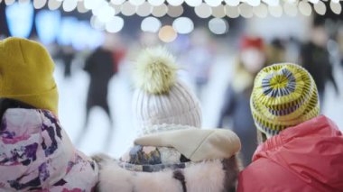 Çocuklar buz pateni pistindeki patencilere bakıyor.