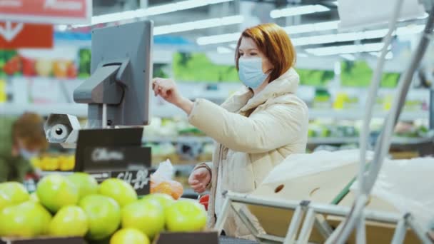 Vrouw in masker weegt fruit in de winkel — Stockvideo