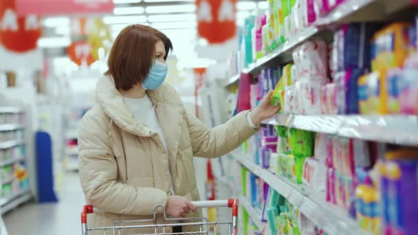 Mulher em máscara escolhendo almofadas menstruais no supermercado — Vídeo de Stock