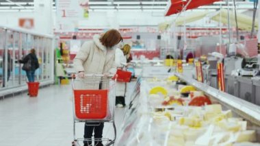 Alışveriş arabalı bir kadın markette peynir vitrinlerinde yürüyor.
