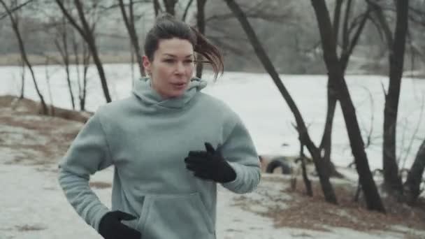 Sportliche Frau joggt im Winter am Seeufer entlang — Stockvideo