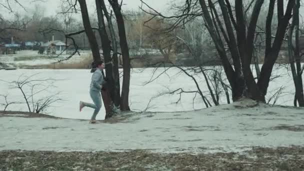 Fitte Frau joggt im Winter am Seeufer — Stockvideo