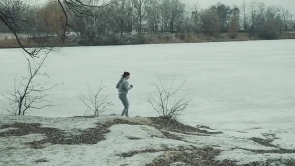 Movimiento lento de la mujer corriendo cerca del lago congelado — Vídeos de Stock