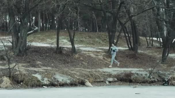 Donna che corre nella foresta invernale vicino al lago ghiacciato — Video Stock