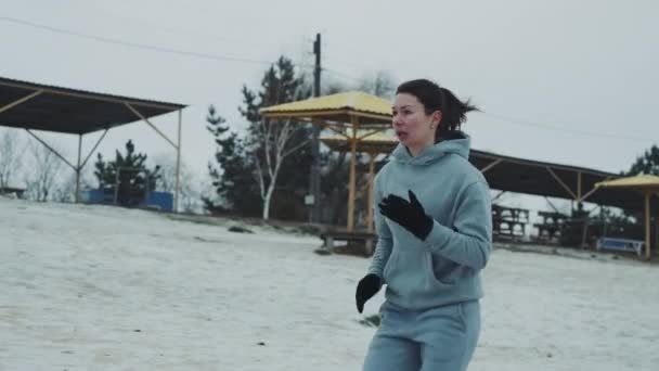 Подходящая женщина бегает по заснеженному пляжу — стоковое видео