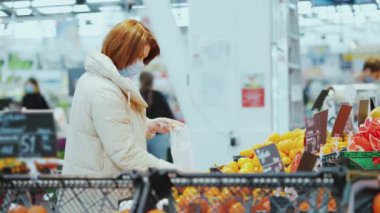 Maskeli kadın alışveriş merkezinde mandalina seçiyor.