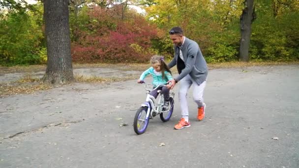 Tata uczy dziewczynkę jeździć na rowerze w parku — Wideo stockowe