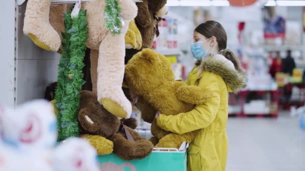 Дівчина в масці вибирає плюшевого ведмедя у відпустці — стокове відео