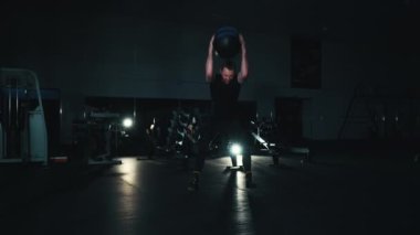 Formda adam karanlık spor salonunda ağır top atıyor.