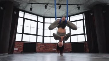 Kadın baş aşağı asılı ve yoga sınıfında meditasyon yapıyor.