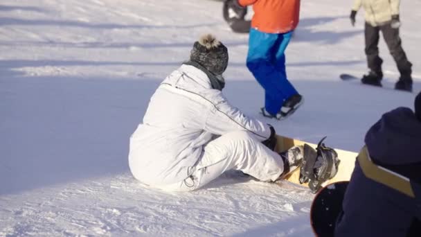 雪の山の上でスノーボードにブーツを取り付ける女性 — ストック動画