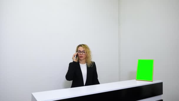 Receptionist die aan de balie staat en telefoneert — Stockvideo