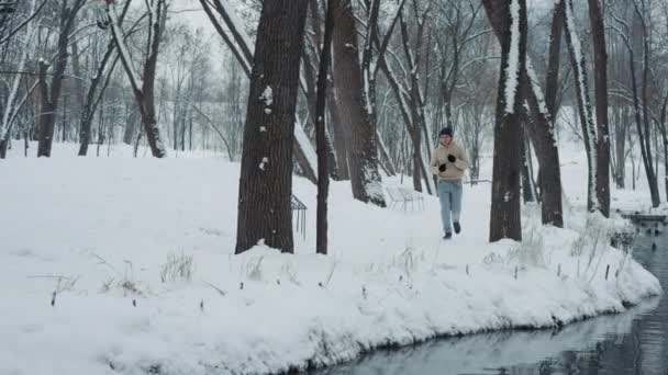 Man joggen op sneeuw langs rivier in park — Stockvideo