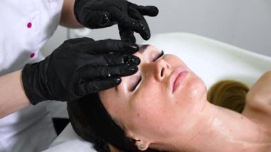 Güzellik uzmanının elleri sağlık spa ziyaretçisinin yüzüne ve boynuna maske takıyor.