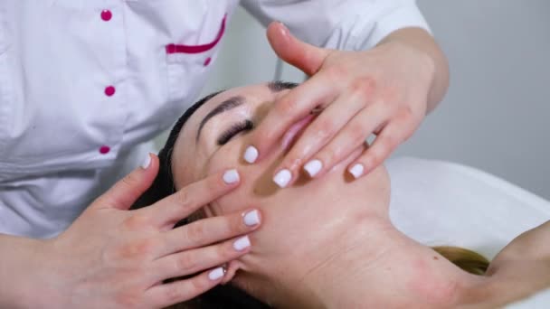 Медленный косметолог делает массаж лица женщине в клинике красоты — стоковое видео