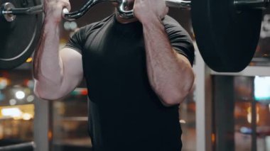 Halterle pencereye doğru egzersiz yapan kaslı bir adam.