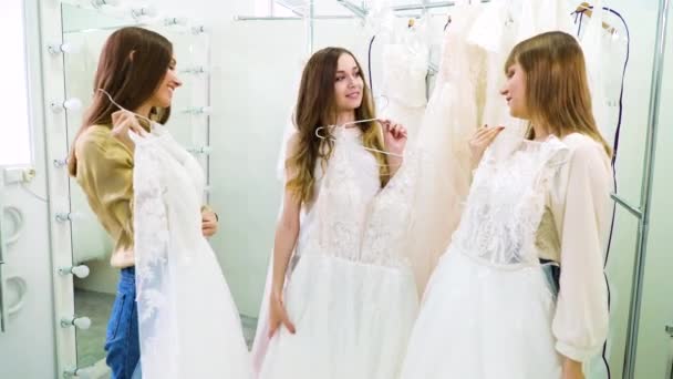 Три жінки намагаються на весільних сукнях у весільному салоні — стокове відео