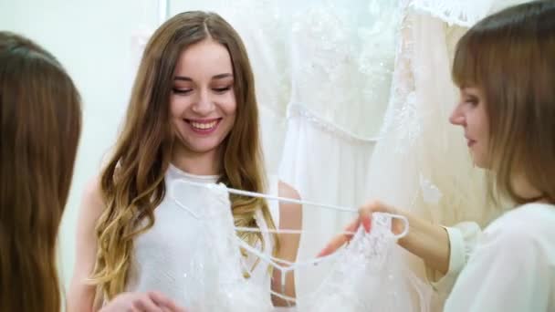 Friends helping future bride to choose wedding dress in salon — Stock Video