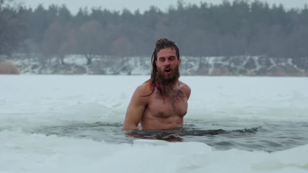 Голый мужчина брызгает водой в ледяную яму — стоковое видео