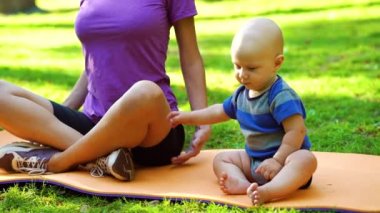 Baby sitting next to mother doing yoga in park