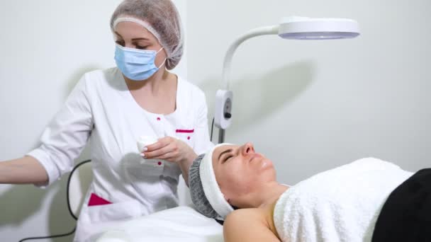 Beautician tillämpa grädde i ansiktet på kvinnliga kunder i wellness salong — Stockvideo