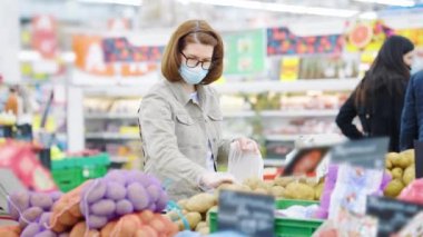 Maskeli kadın dükkanda patatesleri poşete koyuyor.