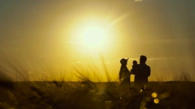 Gün batımında aile ve bebek siluetleri tarlada