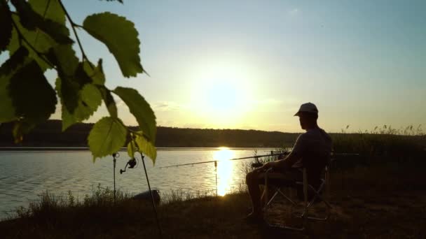 Silhouette di pescatore sulla riva del fiume che beve alcol al tramonto — Video Stock