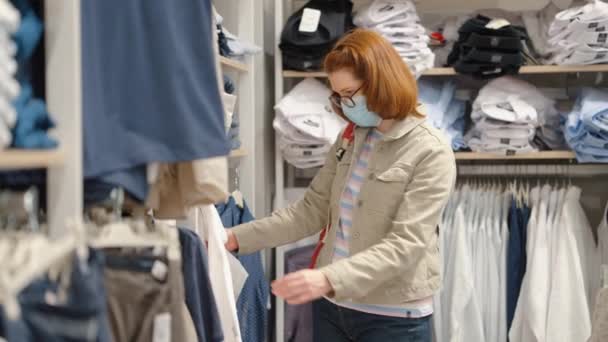 Mujer con máscara eligiendo ropa masculina en el supermercado — Vídeos de Stock