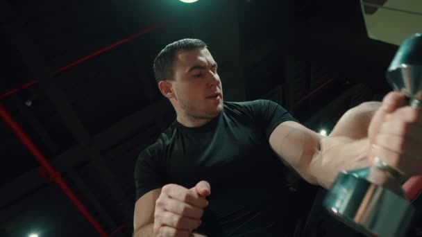 Silny mężczyzna podnoszący hantel i patrzący na bicepsy — Wideo stockowe