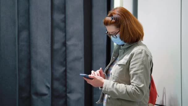 Femme en masque vérifier smartphone tout en se tenant près de vestiaire — Video