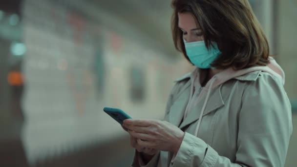 Mujer con máscara usando el teléfono en la plataforma del metro — Vídeo de stock