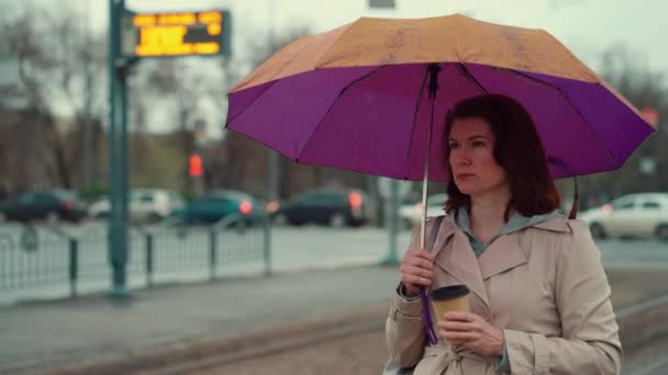 Женщина, стоящая под зонтиком с чашкой кофе — стоковое видео