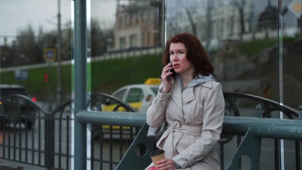 Nő beszél telefonon a buszmegállóban esős időben — Stock videók