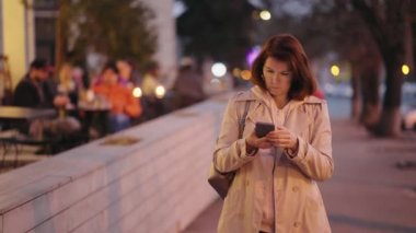 Kadın şehir caddesinde akıllı telefonu kontrol ediyor.