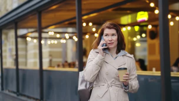 Любитель кофе разговаривает по телефону на городской улице — стоковое видео