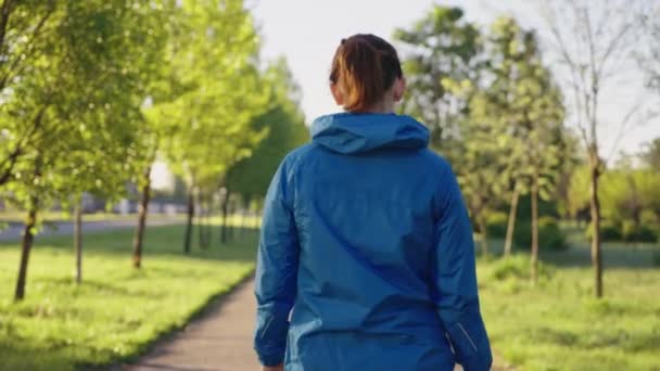 Женщина в спортивной куртке гуляет в парке утром — стоковое видео