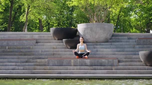 Yogi woman meditating near pond in park — Stock Video