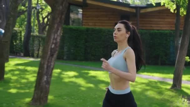 Slow motion vrouwelijke jogger met oortjes in het park — Stockvideo