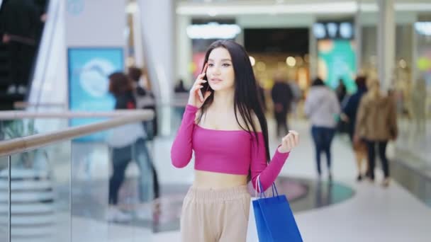 Młoda kobieta z torbami na zakupy rozmawiająca przez telefon — Wideo stockowe