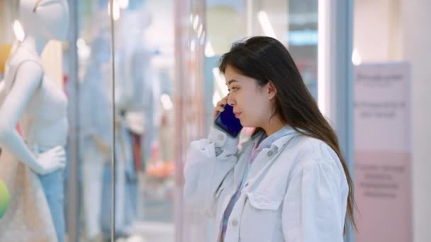 Asyalı kadın vitrinlere bakıyor ve telefonla konuşuyor. — Stok video