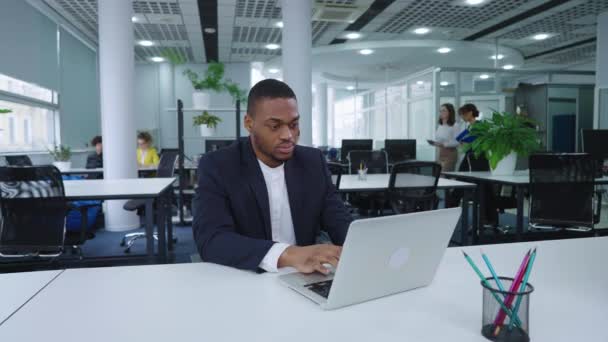 Czarny biznesmen pracujący na laptopie w biurze open space — Wideo stockowe