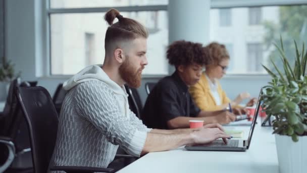 Γενειοφόρος hipster που εργάζονται σε φορητό υπολογιστή στο γραφείο — Αρχείο Βίντεο