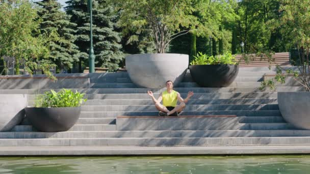 Yogi man meditating near pond in park — Stock Video