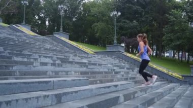 Yavaş çekim zinde bir kadın parkta merdivenlerde koşuyor.