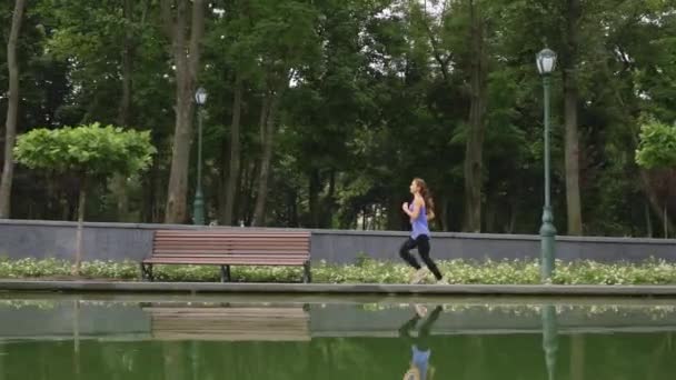 Kvinna som springer nära damm i parken — Stockvideo