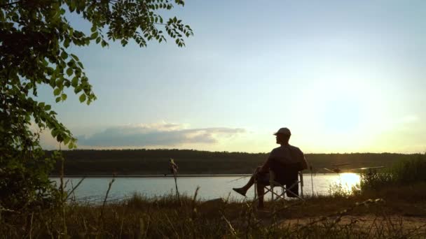 Pescador sentado junto ao rio ao pôr-do-sol — Vídeo de Stock