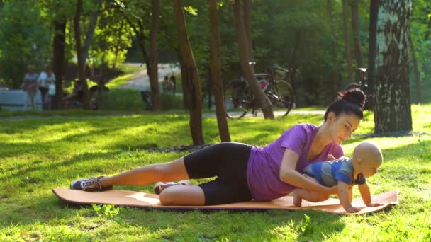 Vrouw doet sport in park met baby spelen naast — Stockvideo