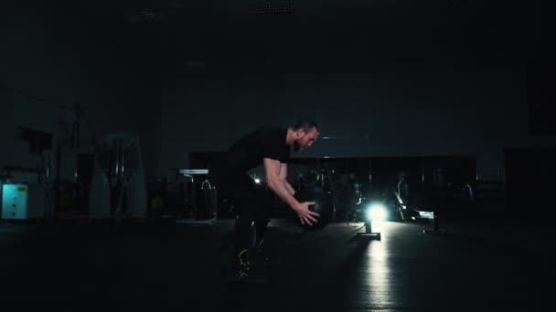 Мужчина тренируется с тяжелым мячом в спортзале — стоковое видео