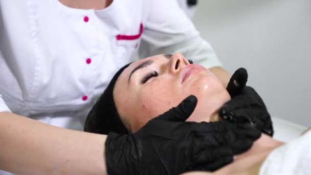 Mãos de esteticista aplicando loção e massageando o rosto da mulher — Vídeo de Stock